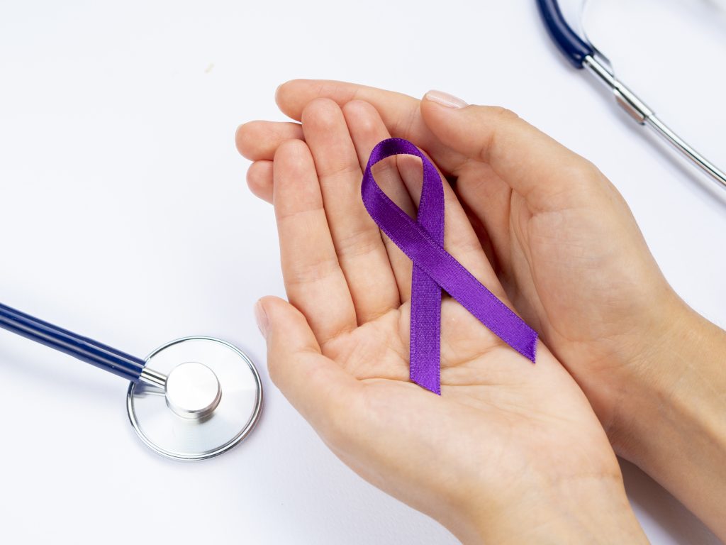 Manos sosteniendo un lazo morado del cáncer. Cómo afrontar un diagnóstico de cáncer.