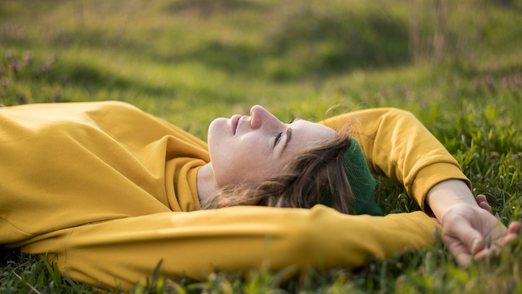 Recomendaciones para hacer frente al estrés. Imagen de mujer relajada tumbada en la hierba. 